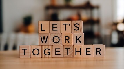 Motivational composition with wooden blocks arranged to spell out the phrase "LETS WORK TOGETHER!". The blocks are placed in a stacked, symmetrical formation on a smooth wooden surface
