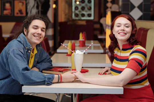 Young couple happily sitting at a retro diner table while holding hands and enjoying milkshakes place has a nostalgic ambiance - Powered by Adobe