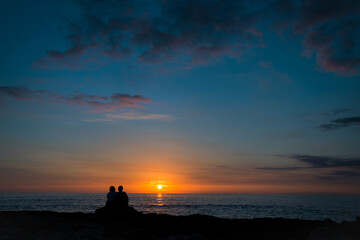Couple sitting by the ocean enjoying the sunset