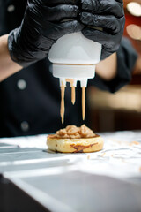 The chef is making a burger, pouring sauce over the delicious burger.
