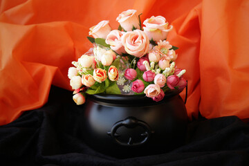 Witch black cauldron used as a vase of flowers on a Halloween decoration table. Black and orange...