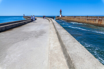 Obraz premium A long concrete pier with a red-topped lighthouse at the end