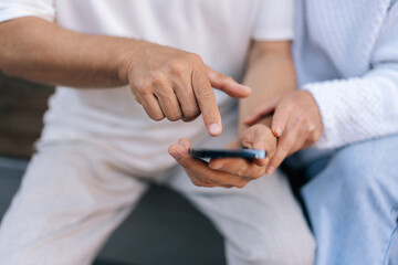 Closeup cropped shot of elderly married couple using smartphone, exploring apps, staying connected with world, embracing digital age in retirement. Senior male and female typing phone together outside