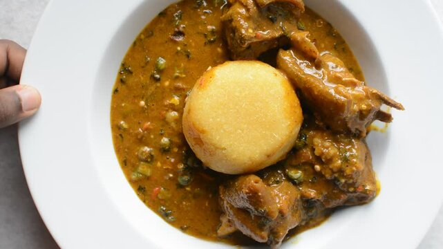 Overhead view of nigerian ogbono soup and eba on a white plate, top view of ogbono draw soup with garri and assorted meats in a soup plate, flatlay of nigerian ogbono and okra soup