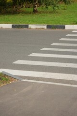 Obraz premium pedestrian crosswalk with white marking lines on asphalt dark road. road markings, zebra crossing, place to cross the road, traffic rules. safety of pedestrians and motorists.