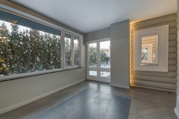 Fototapeta premium A spacious glazed terrace near a wooden log house with a modern design. There .are snow-covered trees outside the window.