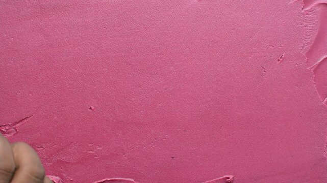 Overhead view of pink silky smooth buttercream being spread with a palette knife, top view of pink frosting being spread