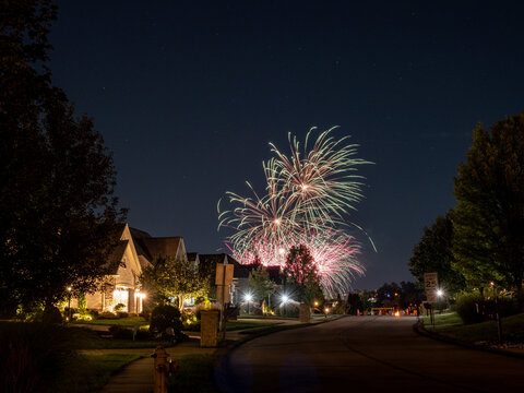 Evening fireworks over an American neighborhood with warm lights.