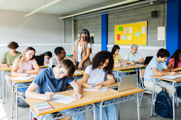 Diverse group of young people doing an academic exam at high school. Mid adult female teacher...