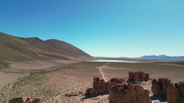Aerial view of the dirt road between the Laguna Vinto high alitude lake and the Italia Perdida volcanic rock formation in Bolivia, on the Andean plateau