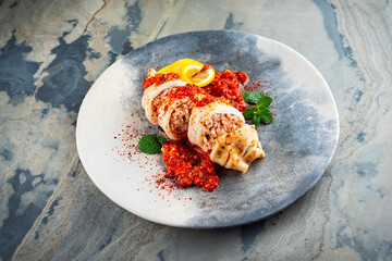 Fried calamari tubes stuffed with rice in salsiccia mince tomato sauce served as close-up on a design plate with copy space