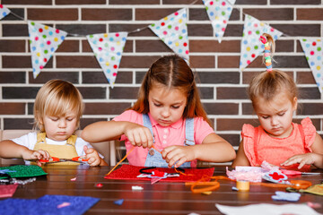 A little toddler boy and two girls cutting something out of beautiful paper at a party