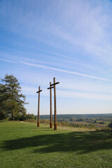 Three wooden crosses standing tall against a clear blue sky on a hill with green landscape and distant hills