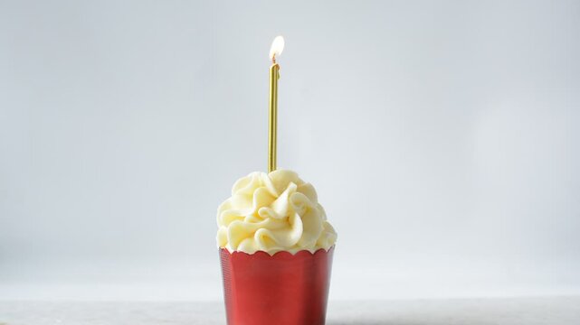 Candle on a red cupcakes being blown out, gold candle on cupcake in red foil liners with vanilla buttercream, frosted cupcakes on a white background