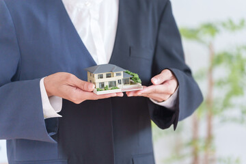 家の模型を持つ不動産営業マン女性
