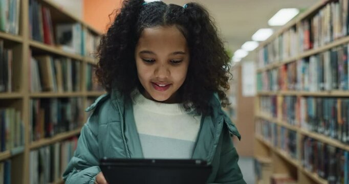 Tablet, kid and happy student in library for education, learning or reading information for knowledge. Tech, girl and child walking at school for studying with ebook for math test preparation online