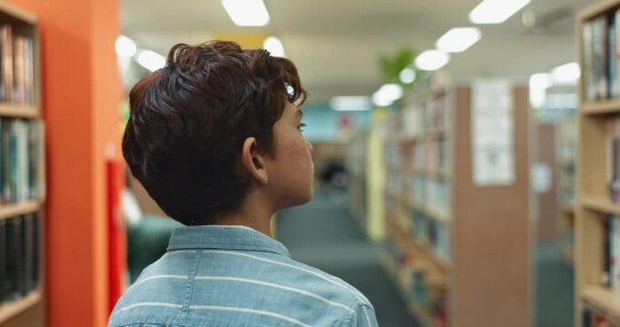Boy, walking and checking library with bookshelf for story, literature or knowledge and learning at bookstore. Young male person or teenager looking at bookcase for education, language or information