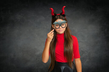 Fototapeta premium child girl with devil horns with funny glasses on Halloween party. Halloween witch teen girl. Little girl witch. Kid witch celebrates Halloween. Portrait of an Halloween child teen girl.