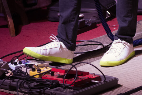 Close-up of a musician's feet operating guitar pedals during a live performance, emphasizing the interaction with the equipment.