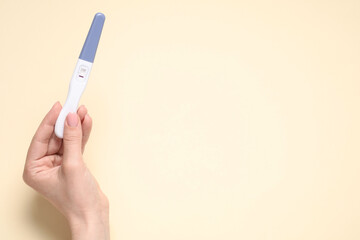 Woman holding pregnancy test on beige background, top view. Space for text