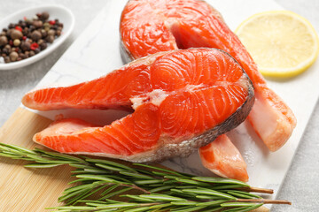 Board with fresh salmon steaks, peppercorns, rosemary and lemon on grey table, closeup