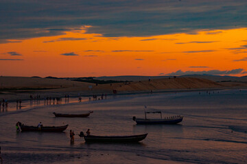 Vibrant sunset over a beach with boats and people silhouetted against orange and blue hues, capturing the lively essence of Jericoacoara.