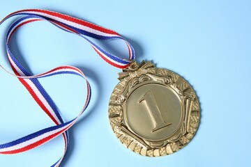 One golden medal on light blue background, top view