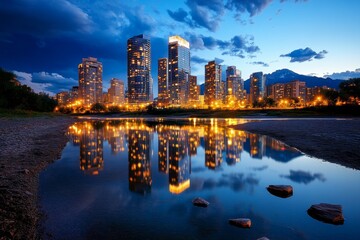 Obraz premium An urban city skyline at night, with skyscrapers lit up against a dark sky, reflecting in a nearby river or lake