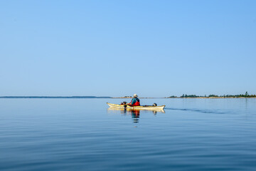 sea kayaker heading out on glass smooth water on a sunny day with blue sky room for text shot on georgian bay ontario in fall