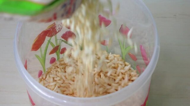 Puffed rice pouring into a plastic container. This popular snack is known by many names, including muri, murmura, kurmura, popped rice, puha, mamra, mandakki, and murmure.
