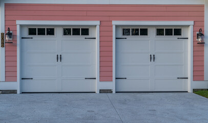 White electronic garage doors transom light windows on a double garage driveway with pink horizontal lap vinyl siding, black powder coated steel spade strap hinge 