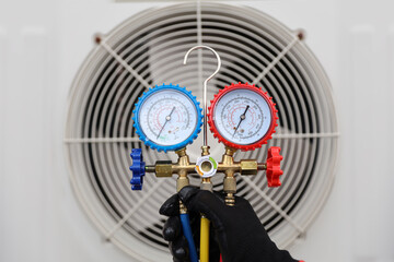 Technician using measuring tool manifold gauge on air conditioning fan for checking refrigerant...