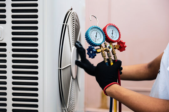 Technician using measuring tool manifold gauge on air conditioning fan for checking refrigerant pump filling home air conditioner and maintenance heat fix repair and clean outdoor compressor unit.