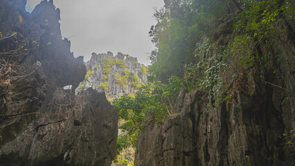 Picturesque karst rocks. Tropical vegetation grows on the steep slopes. Cliff peak is visible through the gap against the sky. Philippines. Palawan.