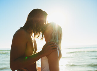 Fototapeta premium Couple, kiss and love on beach outdoor for romance date, sea water and support of tropical vacation. Happy, woman and man with embrace for loyalty, travel together and holiday journey of summer peace