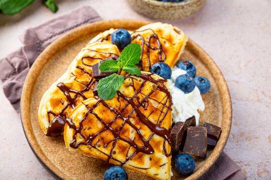 Homemade waffles with blueberries, chocolate sauce and cream cheese in a plate and a beige background