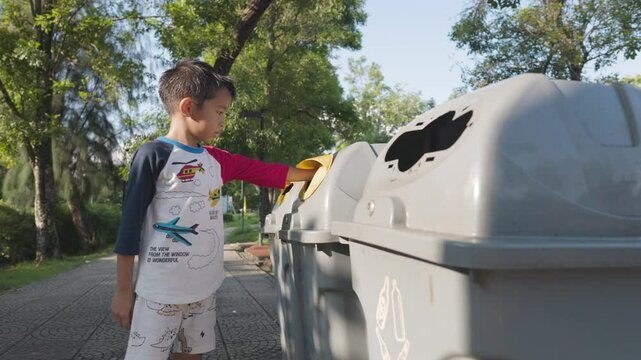 Adorable little boy keep drinking water to trash can garbage bin in public city park
