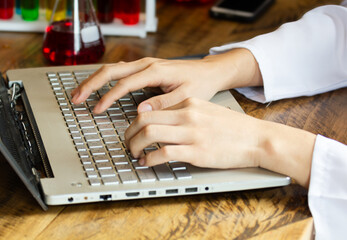 Close up male lab assistant chemist using laptop for data entry and in other hand holding test tube with red blood sample while sitting in central laboratory.