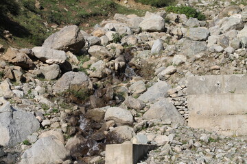 Small pebbles scattered on the ground with a gentle flow of water trickling over them from the mountain.