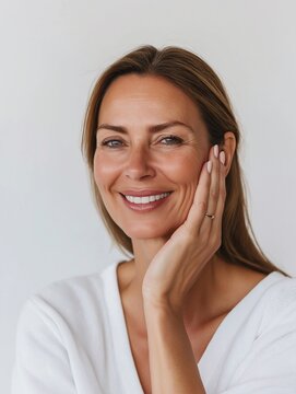 Happy middle aged 40 years old woman applying facial anti age skincare cream on face isolated on white background. Smiling mature beautiful female model advertising skin care product.