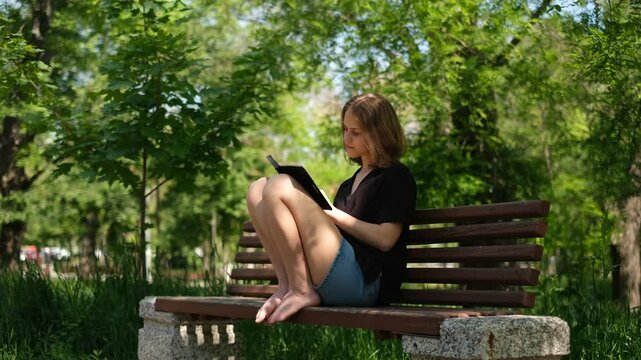 young woman student reading a book in the park on a bench on a sunny summer day