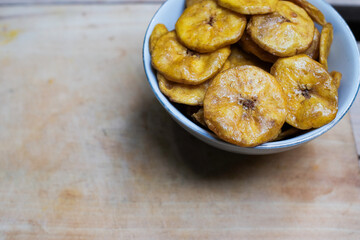 Keripik pisang or banana crackers on a white bowl at wooden cutting board. With copy space. Indonesian traditional snack made from banana and sugar.