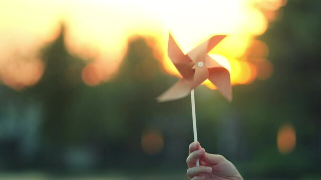 ESG and Clean Energy Concept. Close-up hand of woman holding wind turbine paper in park outdoor at sunset, Produce a green power and decrease carbon, World earth day, Sustainable resources.