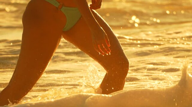 Woman Beach Sunset - A woman walks into the ocean at sunset on a beach.