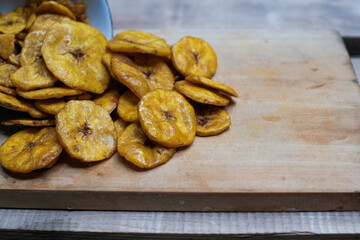 Keripik pisang or banana crackers a white glass jar at wooden cutting board. With copy space. Indonesian traditional snack made from banana and sugar.