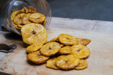 Keripik pisang or banana crackers a white glass jar at wooden cutting board. With copy space.