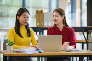 Two young Asian businesswomen discussed investment project work and planning strategy. Business people talk together on laptop computers at the office.