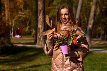 Smiling woman in a pink jacket with a glass of coffee tea in autumn park