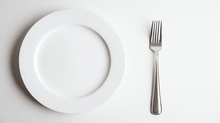 A white plate and a silver fork are on a white background, ready to be used for a meal.