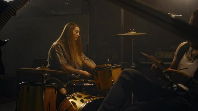 Medium shot of young Caucasian female drummer setting up percussion instruments in company of unrecognizable male music band mates before live performance on stage